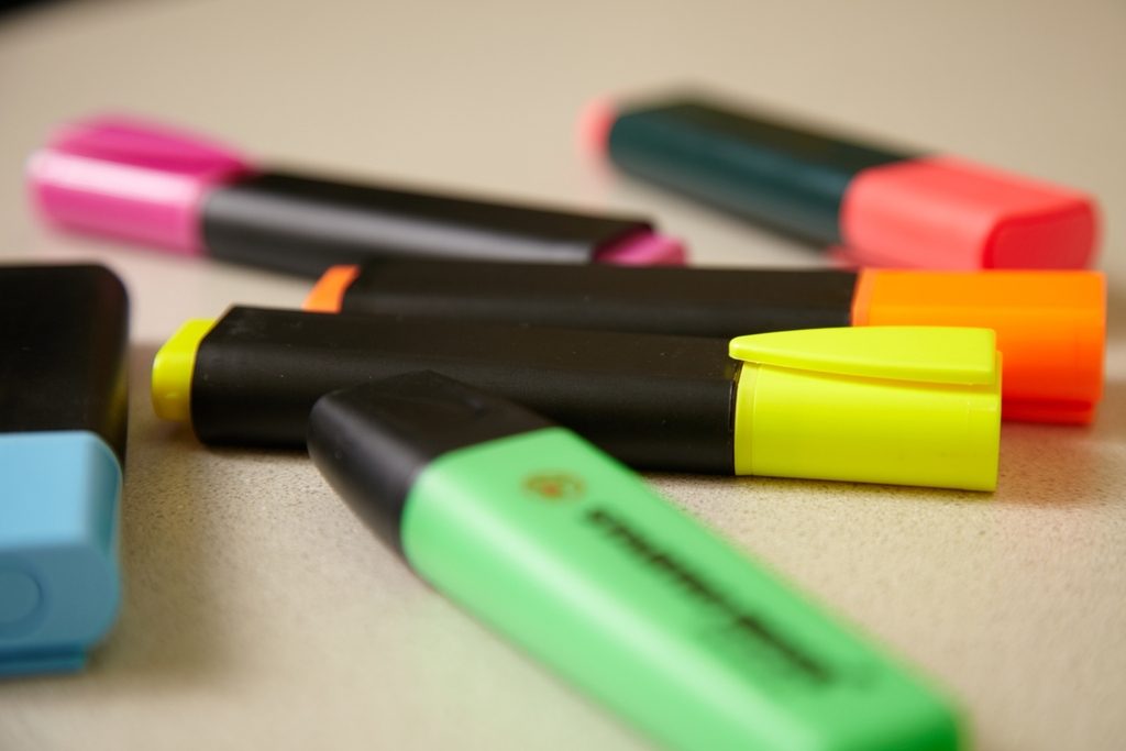 Mehrere bunte Textmarker liegen auf einem hellen Schreibtisch